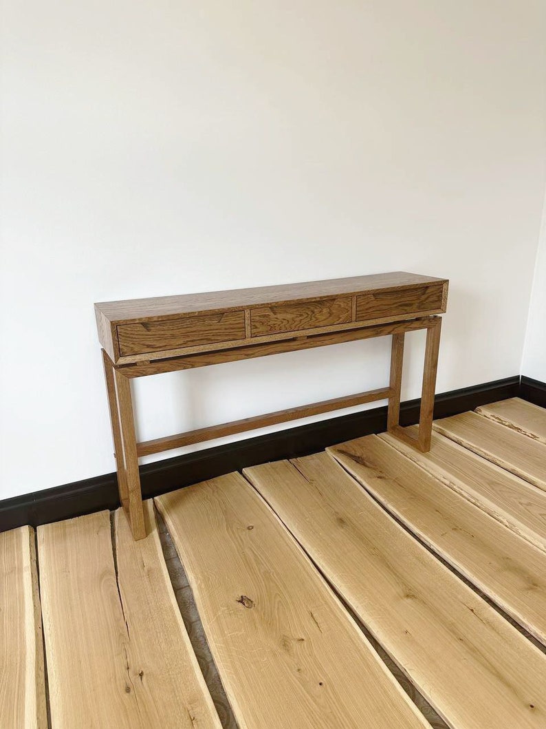 May include: A wooden console table with three drawers and a simple design. The table has a light brown finish and is supported by four legs.