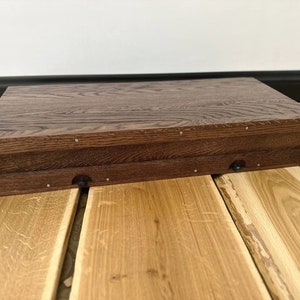 May include: A dark brown wooden box with a hinged lid. The box has a natural wood grain and is closed. The box is sitting on a light brown wooden surface.