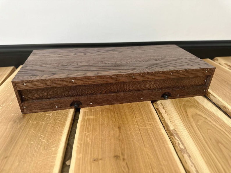 May include: A dark brown wooden box with a hinged lid. The box has a natural wood grain and is closed. The box is sitting on a light brown wooden surface.