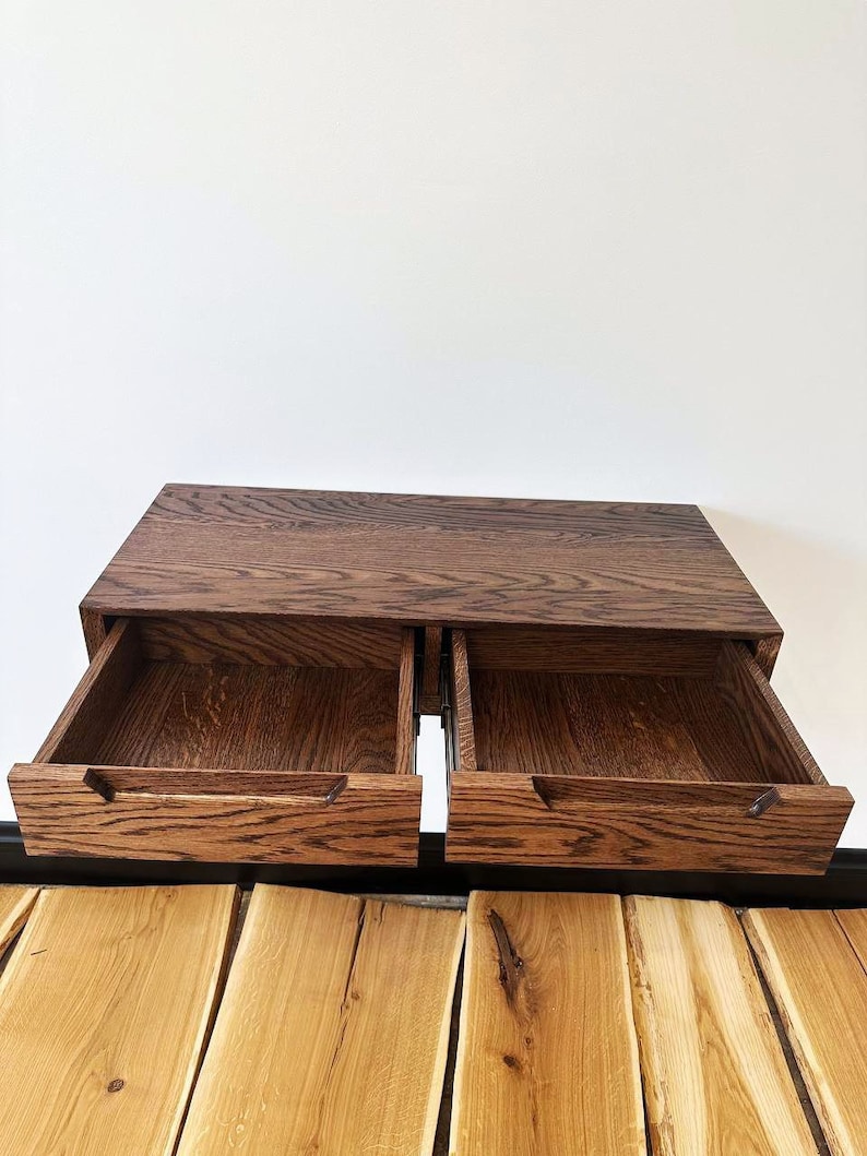 May include: A wooden wall-mounted shelf with two drawers that are open. The shelf is made of dark wood with a grain pattern. The drawers are also made of wood and have a light brown finish.