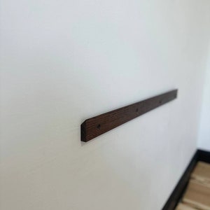 May include: A dark brown wooden shelf mounted on a white wall with four visible screws.