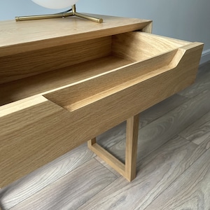 May include: A light wood nightstand with a single drawer that has a cutout handle. The drawer is open and the nightstand is sitting on a light wood floor.