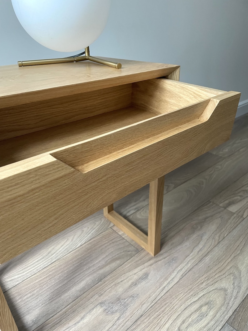 May include: A light wood nightstand with a single drawer that has a cutout handle. The drawer is open and the nightstand is sitting on a light wood floor.