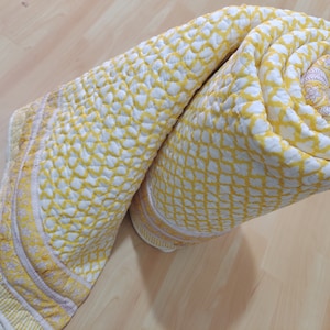 May include: A yellow and white cotton quilt with a geometric pattern. The quilt is rolled up and has a pink and white border.