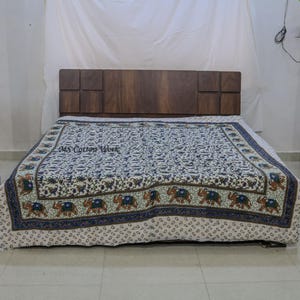 Puede incluir: Una colcha con un estampado de elefantes repetido en tonos azules, marrones y verdes sobre un fondo crema. La colcha está sobre una cama con un cabecero de madera oscura. El texto "MS Cotton Work" es visible en la colcha.