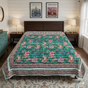 May include: A teal floral quilt with pink and yellow flowers covers a bed. The quilt has a detailed border with pink and green accents. Two framed travel posters hang above the bed, and two lamps sit on the nightstands.