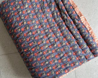 May include: A folded, quilted blanket with a floral pattern. The blanket features a dark blue background with rows of red and green floral designs. The border is striped in orange and white.