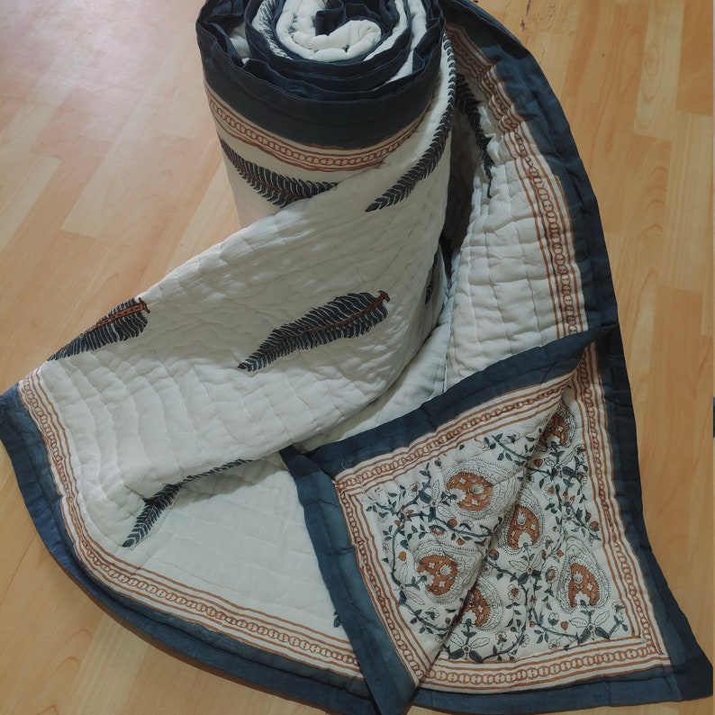 May include: A white cotton quilt with a blue and brown floral print. The quilt is folded and rolled up, showing the blue and brown floral print on the inside.
