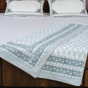 May include: A white and gray patterned cotton quilt with a leaf design. The quilt is folded and displayed on a bed with white pillowcases.