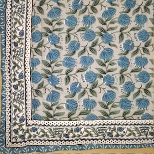 May include: A white cotton quilt with a blue floral pattern. The quilt has a border with a black and white geometric design.