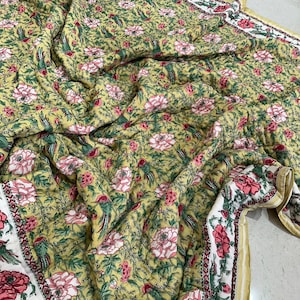 Op de afbeelding: Een geel en groen bloemenpatroon quilt met roze bloemen en groene bladeren. De quilt is gemaakt van katoen en heeft een zacht, comfortabel gevoel.