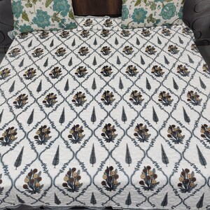 Può includere: Copriletto trapuntato bianco con un motivo ripetuto di bouquet floreali marroni e beige e alberi grigi stilizzati, incorniciati da un disegno a traliccio blu. Sono visibili due cuscini floreali abbinati.