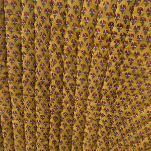 Può includere: Primo piano di un tessuto giallo con un motivo floreale ripetuto in rosso e grigio. La texture trapuntata aggiunge profondità al design. L'estetica generale ricorda i tessuti tradizionali.