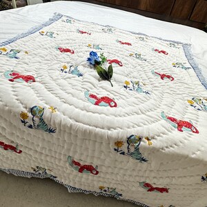 Può includere: Trapunta per neonati in cotone bianco con bordo a righe blu e bianco. La trapunta presenta un motivo ripetuto di tigri rosse e blu e fiori.