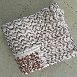 May include: White cotton quilt with a brown chevron pattern and a floral print in the lower right corner.