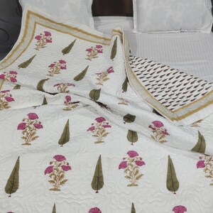 May include: White cotton quilt with a floral print featuring pink flowers and green leaves. The quilt has a gold and brown border.
