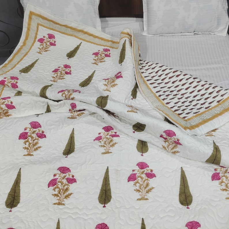 May include: White cotton quilt with a floral print featuring pink flowers and green leaves. The quilt has a gold and brown border.
