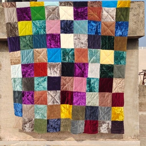 May include: A patchwork quilt with a variety of colors and textures. The quilt is made up of squares of different fabrics, including velvet, satin, and cotton. The quilt is a beautiful example of handmade craftsmanship.