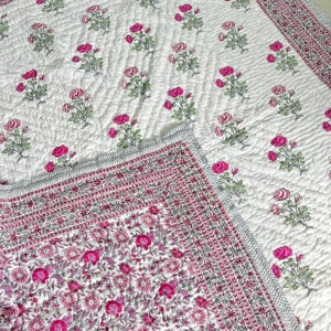 May include: A white cotton quilt with a pink floral print. The quilt has a gray and pink border with a repeating pattern. The quilt is quilted in a diamond pattern.