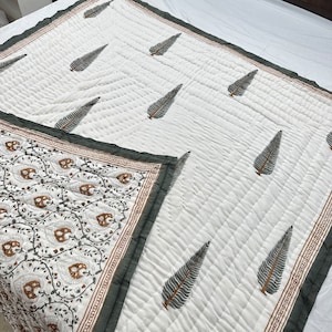May include: A white cotton quilt with a green and brown floral print border. The quilt is quilted with a diamond pattern and features a repeating leaf design in the center.