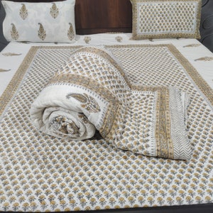 May include: A white cotton quilt with a floral print in shades of grey and yellow. The quilt is rolled up and placed on a bed with matching pillowcases.