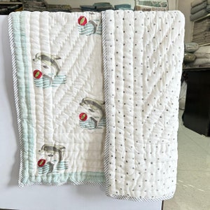 Può includere: Trapunta in cotone bianco con un bordo blu chiaro e verde. Un lato presenta un motivo ripetitivo di delfini che saltano sopra una palla rossa. L'altro lato ha uno sfondo bianco con piccoli pois grigi.