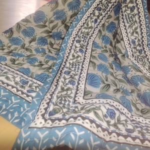 May include: A blue and white patterned fabric with a floral design. The fabric has a quilted texture and a border with a geometric pattern.