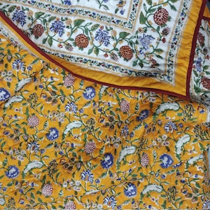 Pode incluir: Uma colcha com padrão floral amarelo e branco com uma borda vermelha. A colcha é feita de algodão e é perfeita para adicionar um toque de estilo tradicional a qualquer quarto.