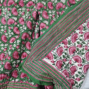 May include: A green and pink floral patterned quilt with a white border and green stripes. The quilt is folded in half, showing both sides of the fabric.