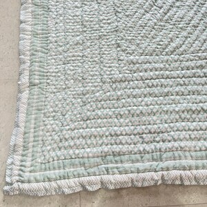 May include: A green and white quilted throw blanket with a ruffled edge. The blanket has a small floral pattern and a chevron pattern on the border.