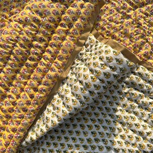 Può includere: Una trapunta reversibile con un motivo floreale giallo da un lato e un motivo floreale bianco dall'altro. La trapunta ha un bordo marrone ed è realizzata in un tessuto trapuntato morbido. Il motivo floreale presenta accenti rossi, gialli e verdi.