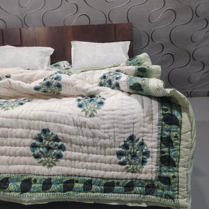 Può includere: Un piumino di cotone bianco con stampa floreale verde e blu. Il piumino ha un motivo trapuntato e un bordo verde e nero.