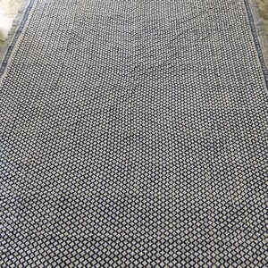 May include: A rectangular textile featuring a repeating dark blue and white diamond grid pattern across the centre. The border consists of a dark blue floral motif on a white background, finished with a thin, dark blue and white striped edge.