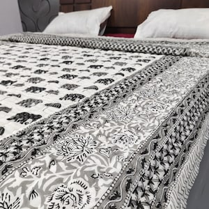 Puede incluir: Una colcha de algodón blanco con estampado floral en blanco y negro. La colcha tiene un borde de elefantes blancos y negros.