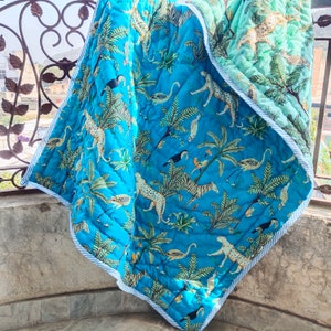 May include: A blue and green reversible quilt with a jungle animal print. One side features a blue background with white stripes and the other side features a green background with white stripes. The quilt features a variety of animals including zebras, leopards, and birds.