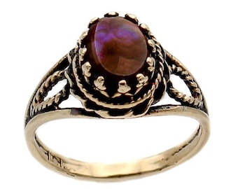 May include: A silver ring with an oval, iridescent gemstone. The gemstone has shades of purple and brown. The ring features a decorative, openwork design around the stone and a twisted rope pattern on the band.