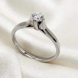 May include: A solitaire engagement ring featuring a round diamond set in a silver band. The diamond is the focal point, sparkling brightly. The band has a classic, elegant design.