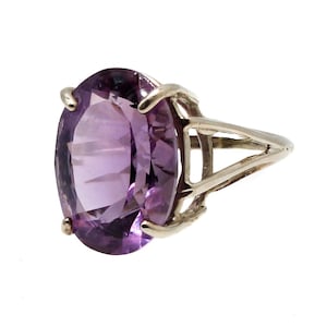 May include: A silver ring featuring a large, oval-cut amethyst gemstone. The amethyst is a deep purple color and is set in a four-prong setting. The ring has a split shank design.