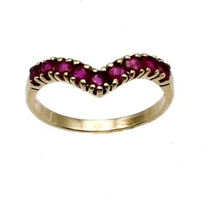 May include: A gold-toned ring with a V-shaped design, set with multiple small, round, deep red gemstones. The ring's band is smooth and polished, and the gemstones are closely set together.