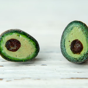Può includere: Due metà di avocado dipinte su legno, con vernice verde e marrone, su una superficie di legno bianco.