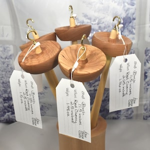 May include: A collection of wooden drop spindles with brass hooks and attached tags. The spindles are made of light brown wood and have a circular top. The tags include measurements of 11.5 inches and 2.25 inches.