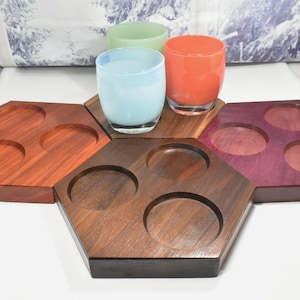 May include: A collection of wooden drink coasters in various colors, including red, brown, and purple. Each coaster has circular indentations to hold glasses. Three colorful glass tumblers sit on top.
