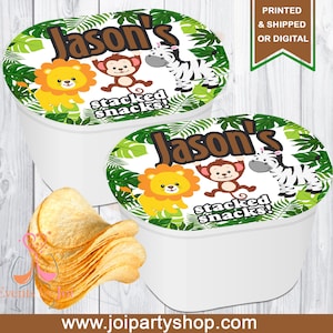 May include: Two white containers with lids featuring a jungle-themed design. The lids have a green leaf border, the name "Jason's", and cartoon animals. The text "stacked snacks!" is also visible. A pile of potato chips is in the foreground.