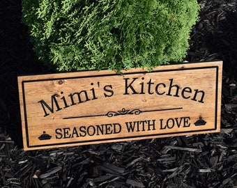 May include: A wooden sign with the text "Mimi's Kitchen" and "Seasoned with Love" in black lettering. The sign has a decorative flourish and a pie icon.