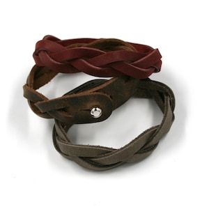 Könnte beinhalten: Drei geflochtene Lederarmbänder in Braun, Dunkelbraun und Burgunderrot. Die Armbänder sind übereinander gestapelt.