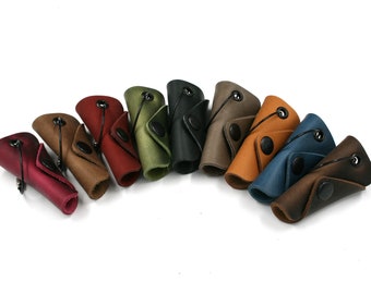 May include: A set of ten leather key holders in various colours, including red, brown, green, blue, and grey. Each holder has a small black button and a loop for attaching keys.