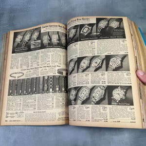 May include: A vintage catalog page featuring a selection of jeweled American-made wristwatches. The page includes a variety of styles, including shockproof, jeweled, and sweep second timer watches. The catalog page also features a variety of watch bands, including a smart new band that makes your old watch look new.