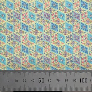 May include: A close-up of a fabric with a repeating pattern of blue, pink, and yellow geometric shapes. A ruler is visible at the bottom of the image, with markings up to 100cm.