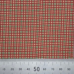 May include: Close-up of a fabric with a red and green plaid pattern. The fabric has a grid-like design with alternating red and green lines. A ruler is placed at the bottom, showing measurements in centimetres.