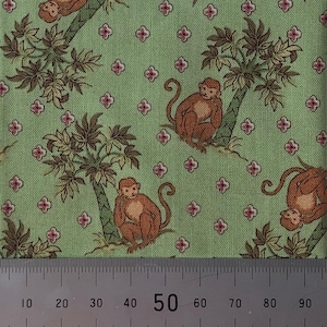 May include: Green fabric featuring a repeating pattern of brown monkeys, palm trees, and pink floral accents. The monkeys are in different poses, some sitting and some hanging from the trees. The fabric has a vintage or retro feel.